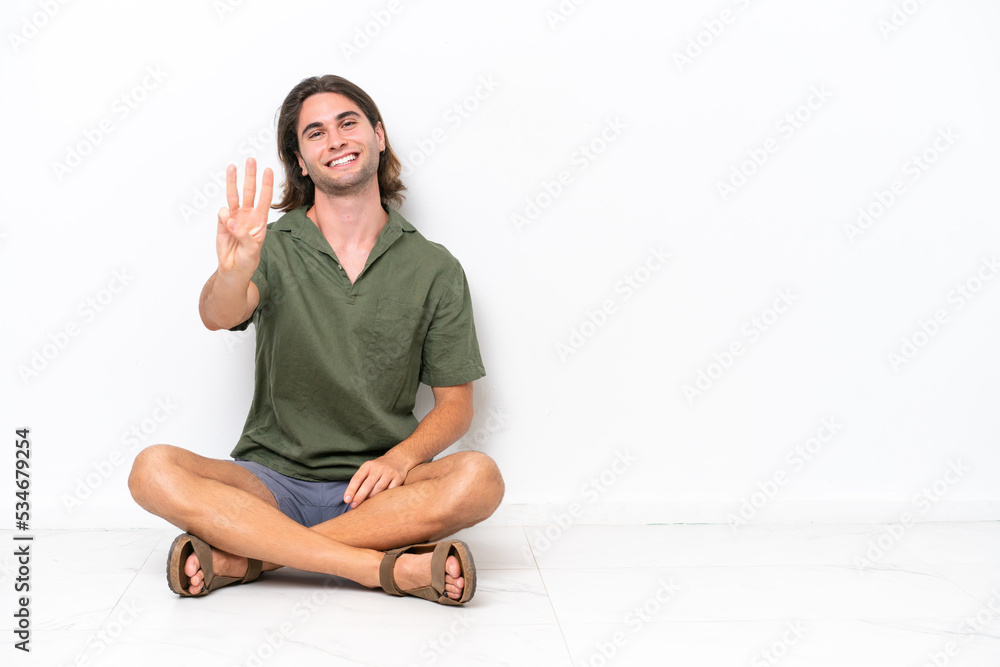 Young handsome man sitting on the floor isolated on white background happy and counting three with fingers