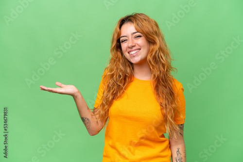 Young caucasian woman isolated on green screen chroma key background holding copyspace imaginary on the palm to insert an ad