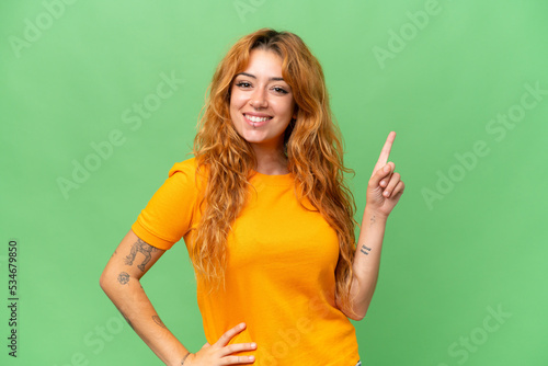 Young caucasian woman isolated on green screen chroma key background showing and lifting a finger in sign of the best
