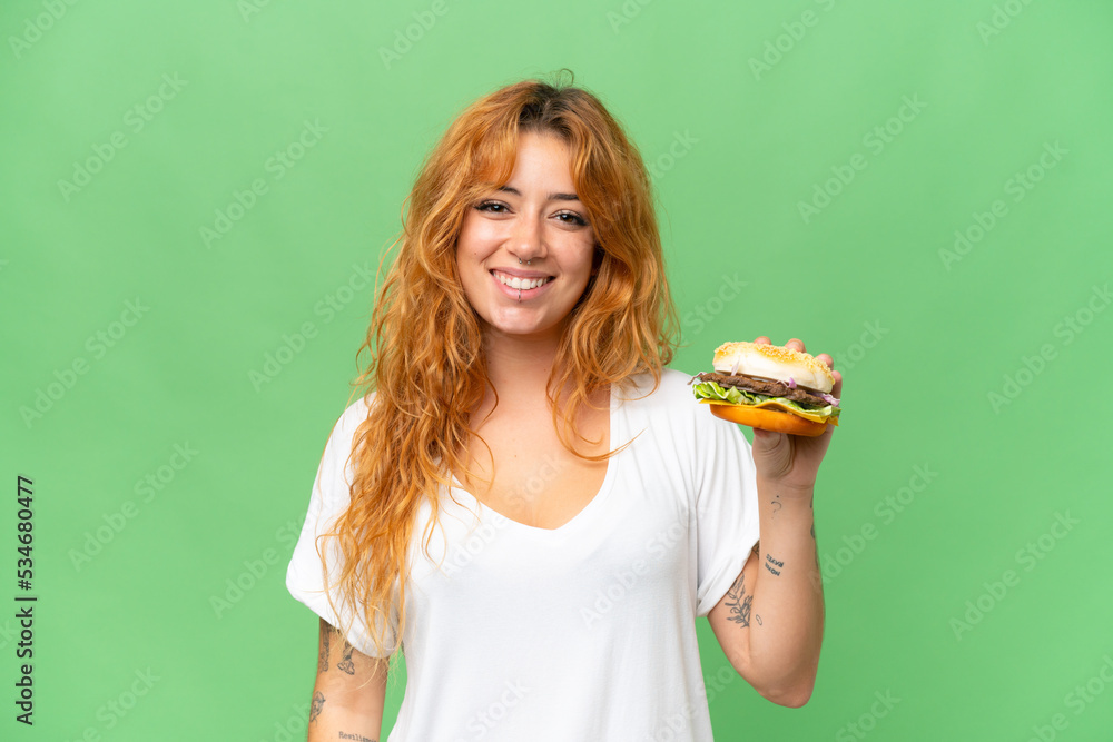 Young caucasian woman holding a burger isolated on green screen chroma key background smiling a lot Young caucasian woman holding a burger isolated on green screen chroma key background smiling a lot