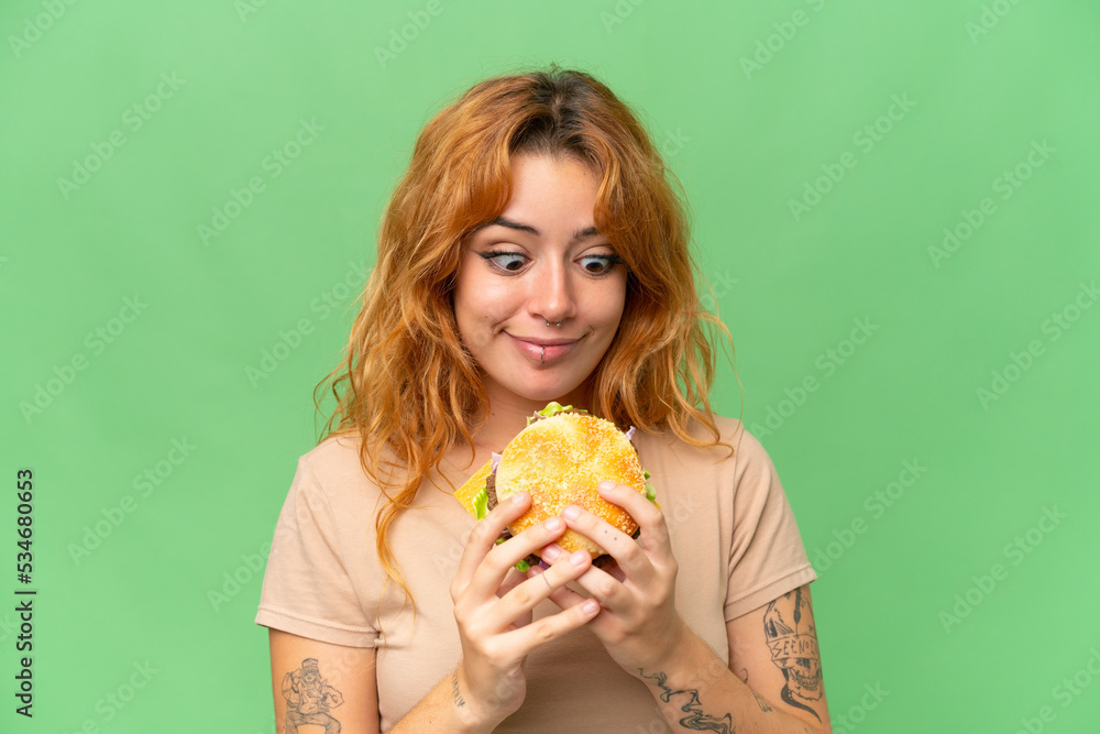 Young caucasian woman holding a burger isolated on green screen chroma key background Young caucasian woman holding a burger isolated on green screen chroma key background