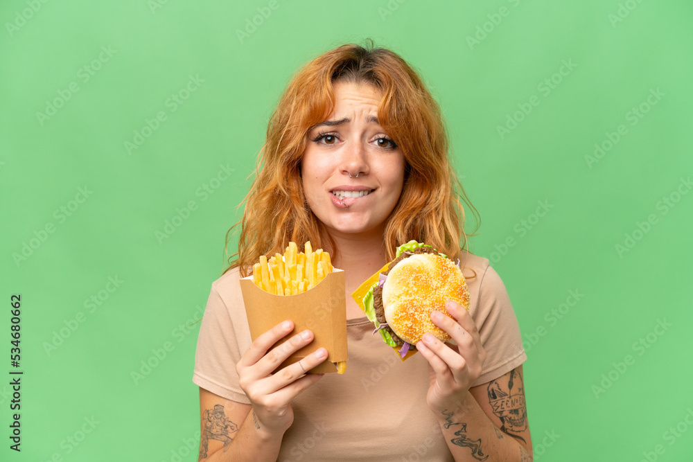 Young caucasian woman holding fried chips and burger isolated on green screen chroma key background