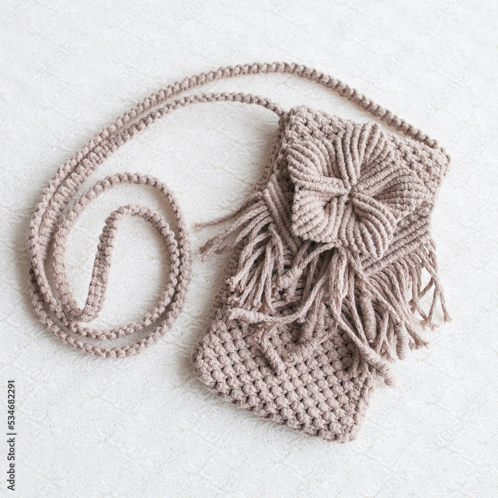 Fototapeta premium Handmade macrame phone bag. ECO friendly natural macrame cotton bag for woman. Hobby knitting handmade macrame. Modern summer concept for woman.