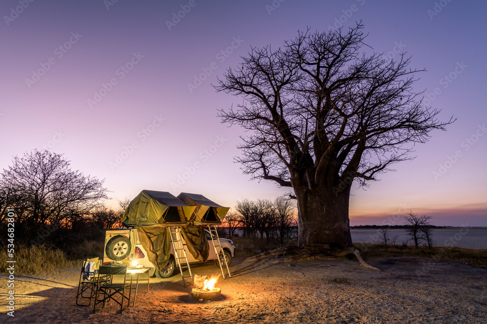 Africa - Camping in the wilderness with fire and sundowner in front of a Baobab Tree, Nxai Pan, Botswana - obrazy, fototapety, plakaty 