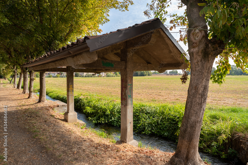 Ancient wash house with canopy on stream bank in the Italian countryside Ancient wash house with canopy on stream bank in the Italian countryside