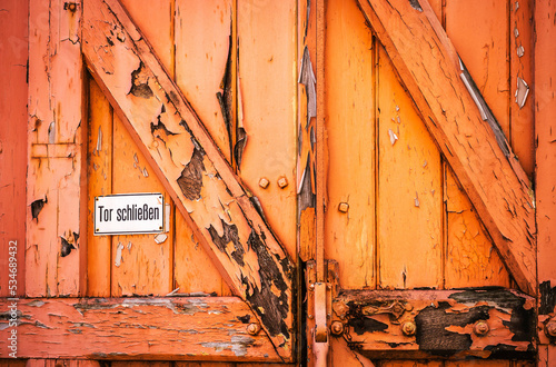 Alte, verwitterte, orangefarbene Holztür mit Hinweis 