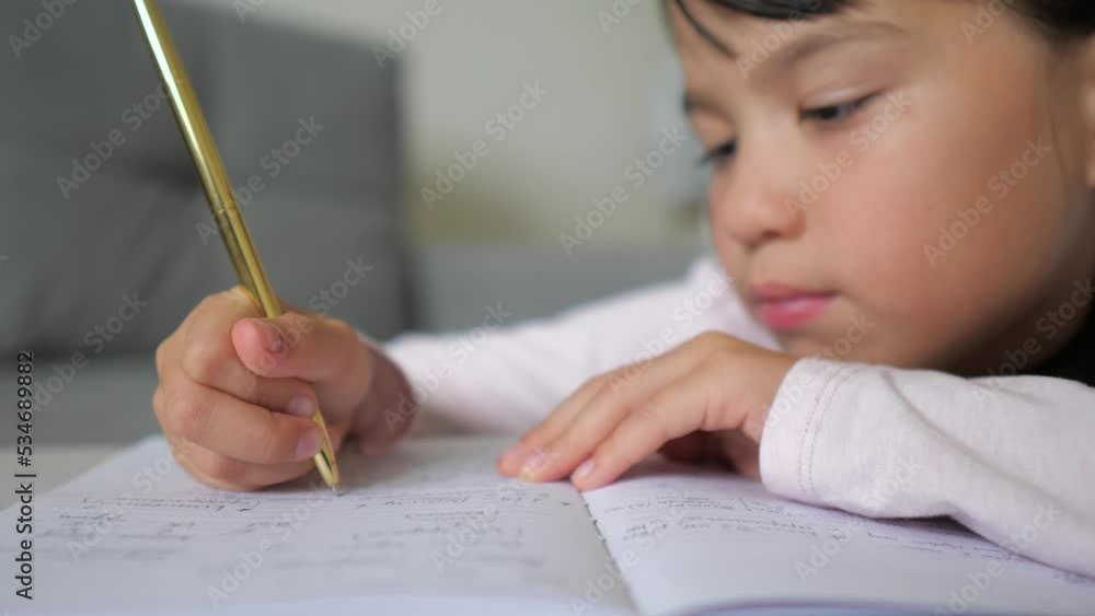 Little girl is writing the essay in notebook at home. Online learning, homeschooling. Kid is doing homework concept. Selective focus Little girl is writing the essay in notebook at home. Online learning, homeschooling. Kid is doing homework concept. Selective focus