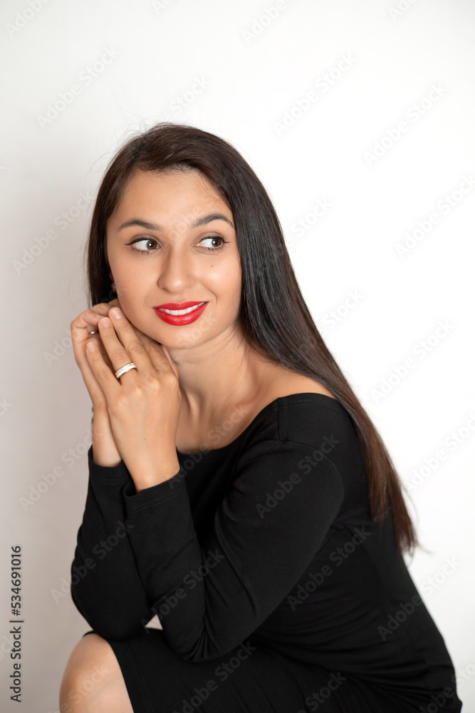 A sensual studio portrait of a beautiful young woman in a black dress with red lipstick on her lips. White background place for text A sensual studio portrait of a beautiful young woman in a black dress with red lipstick on her lips. White background place for text