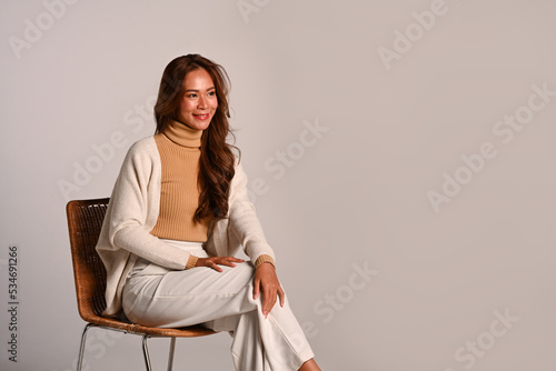 Gorgeous woman wearing stylish trendy clothes in earth tones sitting on beige background. Autumn and Winter concept