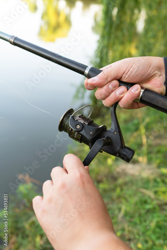 Fishing Reel. The guy spins the coil on the background of the lake. The concept of relaxation and hobby for the soul.