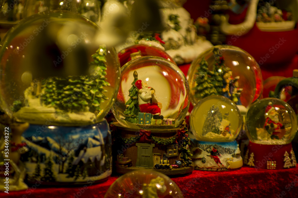 Fototapeta premium Advent Bazaar Stalls with glass, wooden, ceramic christmas souvenirs in shops. Close up of festive decorations for tree in winter street night market during new year's holiday. Illuminated fair kiosk