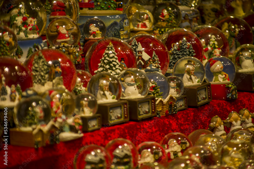 Advent Bazaar Stalls with glass, wooden, ceramic christmas souvenirs in a shop. Close up of festive decorations for tree in winter street night market during new year's holiday. Illuminated fair kiosk