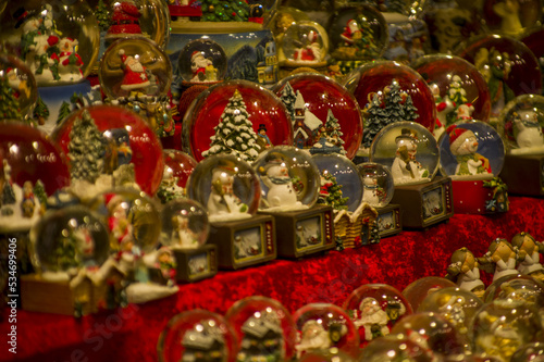 Advent Bazaar Stalls with glass, wooden, ceramic christmas souvenirs in a shop. Close up of festive decorations for tree in winter street night market during new year's holiday. Illuminated fair kiosk
