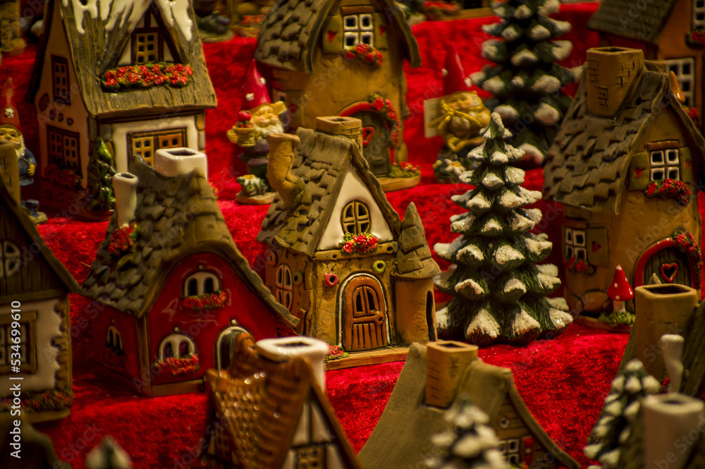 Fototapeta premium Advent Bazaar Stalls with glass, wooden, ceramic christmas souvenirs in a shop. Close up of festive decorations for tree in winter street night market during new year's holiday. Illuminated fair kiosk