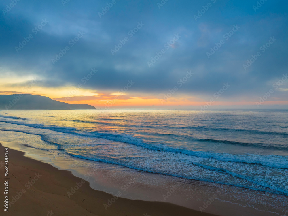 Peaceful sunrise over the ocean with small waves and clouds