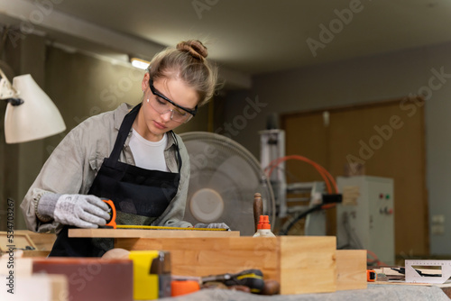 Portrait of a female carpenter measuring the dimensions of the wood prepared for her furniture creation in a furniture factory. with many tools and wood