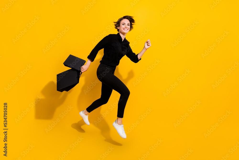 Photo of sweet charming girl dressed formal shirt jumping high holding bags running empty space isolated yellow color background