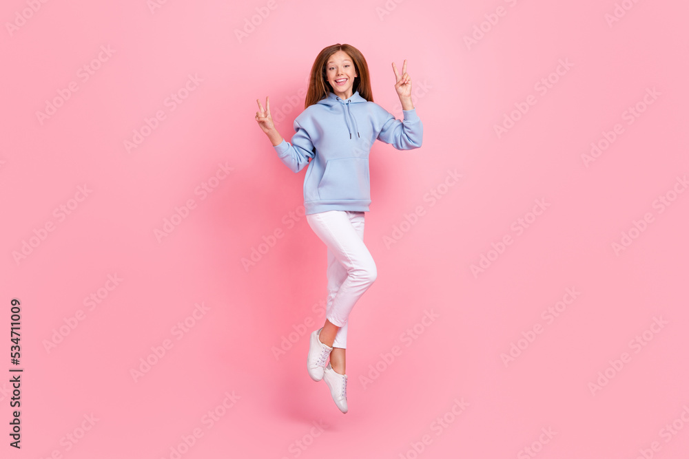 Full body portrait of overjoyed cheerful girl jumping demonstrate v-sign isolated on pink color background