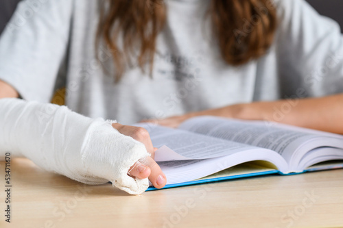 A teenage girl with a hand injury reads a book. Close-up of a bandaged hand on a book. Selective focus on fingers and hand.