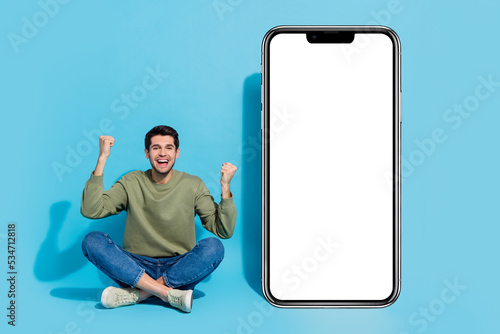 Full body portrait of delighted person sit floor raise fists celebrate success isolated on blue color background