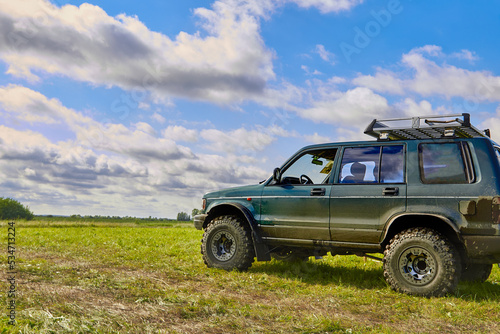 Concept of extreme travel, adventure or tourism in picturesque placesA 4x4 off-road car stands in a meadow against a beautiful blue sky with clouds. 