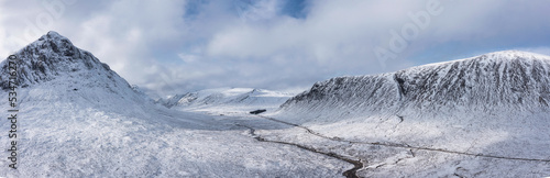 Epic aerial drone panoramic landscape image of Stob Dearg and Glencoe in Scottish Highlands during deep snowfall and beautiful blue skies