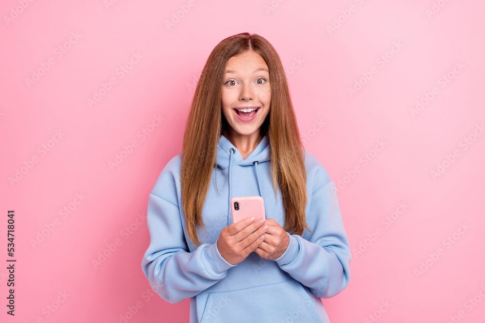 Photo of young funny excited girl wear blue hoodie hold smartphone reaction unexpected blogger youtube much followers isolated on pink color background Photo of young funny excited girl wear blue hoodie hold smartphone reaction unexpected blogger youtube much followers isolated on pink color background