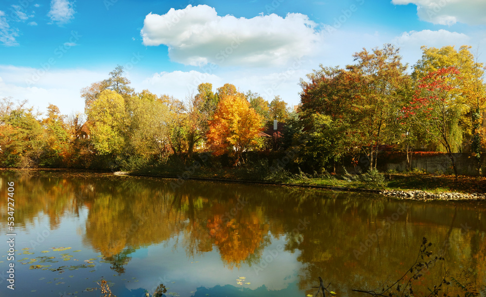 beautiful autumn day with landscape with a lake, colorful trees, cloudy sky and reflection of autumn tree colors on water