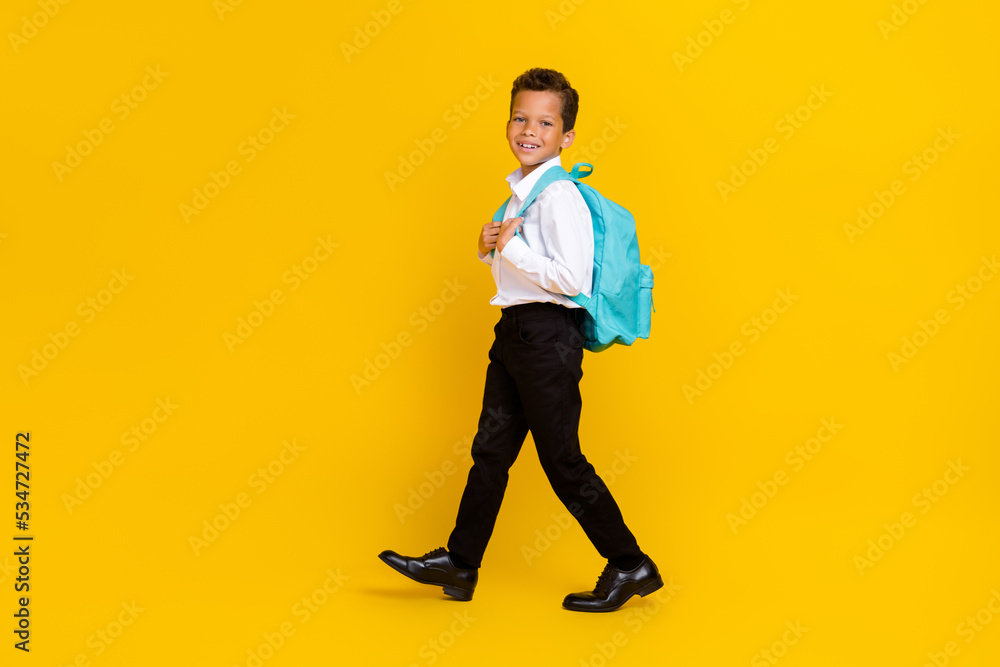 Full body profile photo of positive boy walking carry backpack isolated on yellow color background Full body profile photo of positive boy walking carry backpack isolated on yellow color background