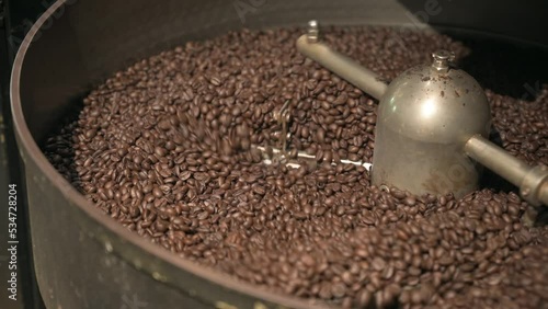 Close up brown coffee bean roasting in a coffee roasting machine with rotating metal arm in 4k.