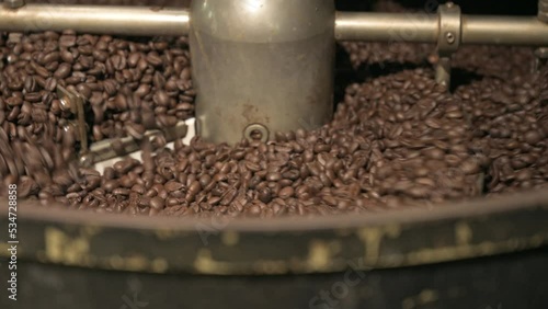 Close up brown coffee bean roasting in a coffee roasting machine with rotating metal arm in 4k.