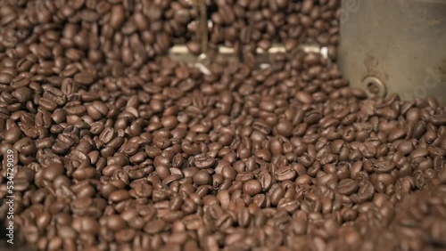 Close up brown coffee bean roasting in a coffee roasting machine with rotating metal arm in slow motion.
