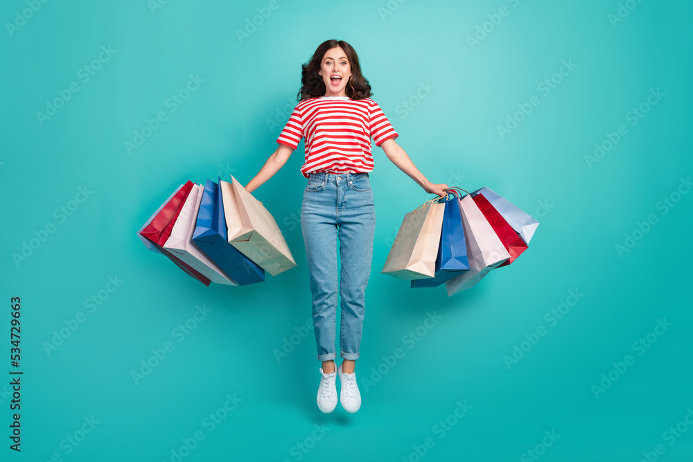 Full length photo of adorable excited girl dressed red t-shirt jumping high holding shoppers isolated teal color background Full length photo of adorable excited girl dressed red t-shirt jumping high holding shoppers isolated teal color background