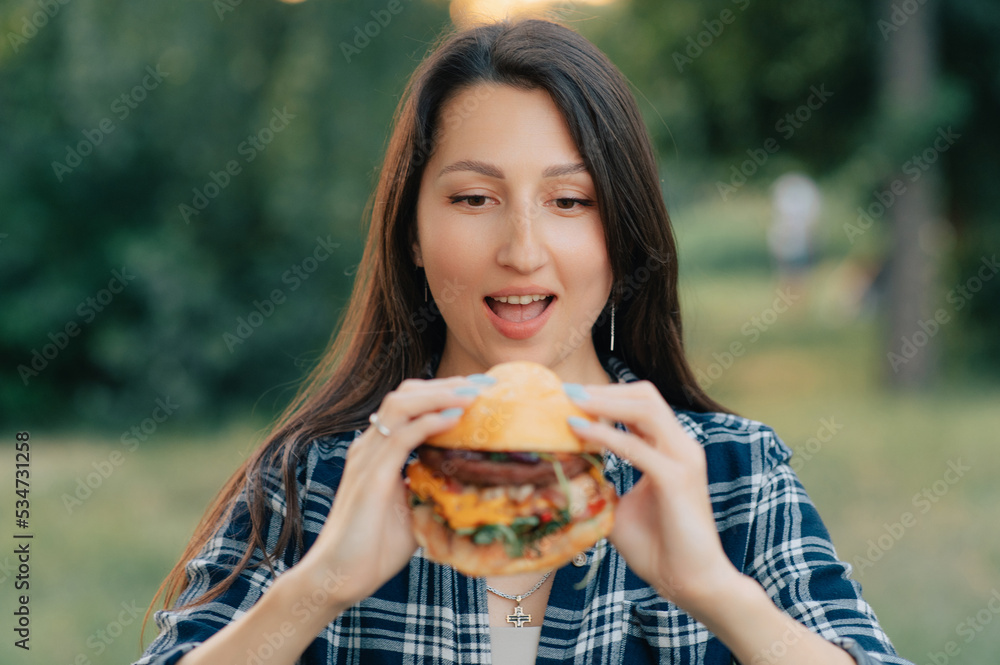 Young attractive hungry woman bites a big hamburger outdoor. Close up. Young attractive hungry woman bites a big hamburger outdoor. Close up.