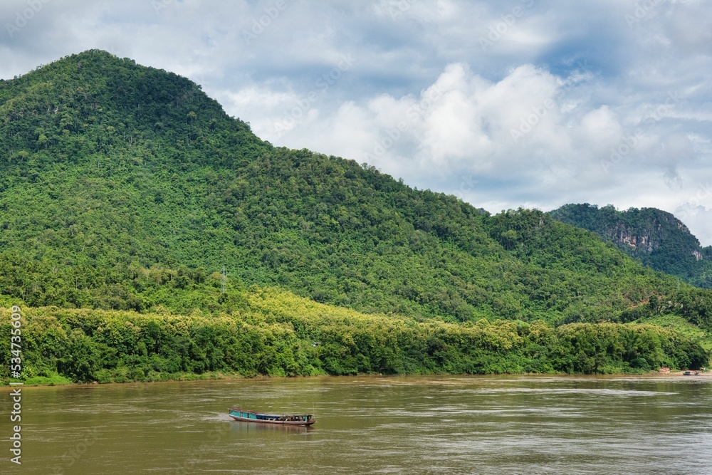 Long Boat travels down the Mekong River at Luang Prabang, beatiful river beetwen mountain forest Long Boat travels down the Mekong River at Luang Prabang, beatiful river beetwen mountain forest
