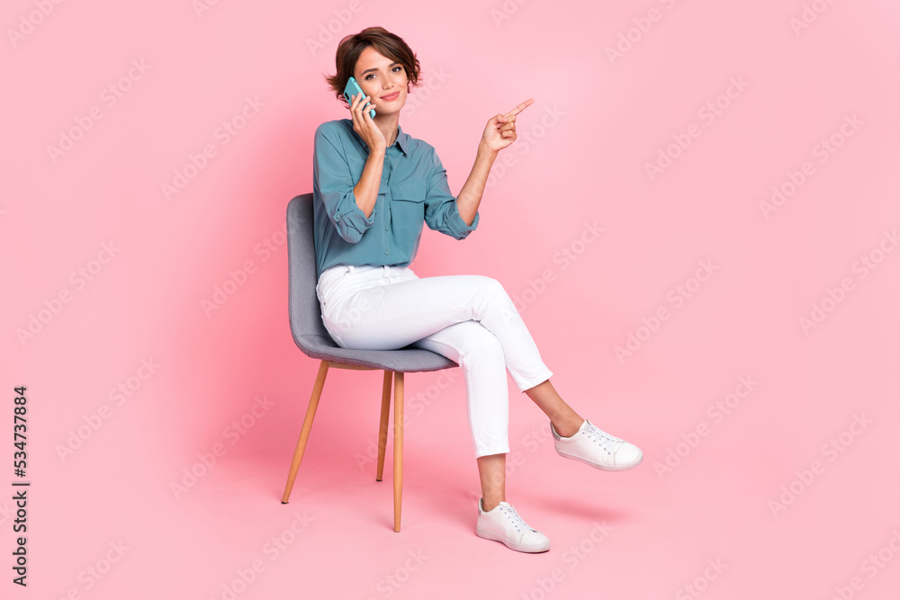 Photo of pretty calm lady sit chair finger direct empty space offer buy modern telephone device gadget isolated on pink color background Photo of pretty calm lady sit chair finger direct empty space offer buy modern telephone device gadget isolated on pink color background