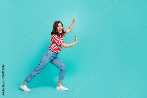 Full length photo of positive lady hold empty space push imaginary stone large product isolated on aquamarine color background