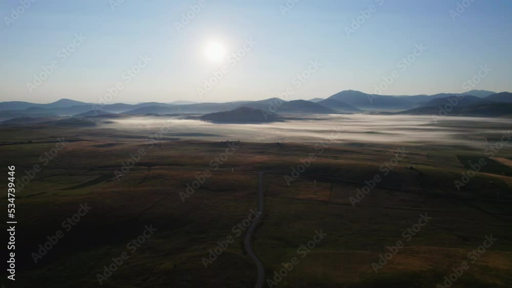Aerial shot at dawn from the mountaintops towards the valley showing low fog and the rising sun, the drone moves in panorama shooting, edited with minimal color correction Aerial shot at dawn from the mountaintops towards the valley showing low fog and the rising sun, the drone moves in panorama shooting, edited with minimal color correction