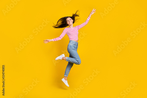 Full length photo of cheerful gorgeous girl wear striped long sleeve jeans arms plane wings flying isolated on yellow color background