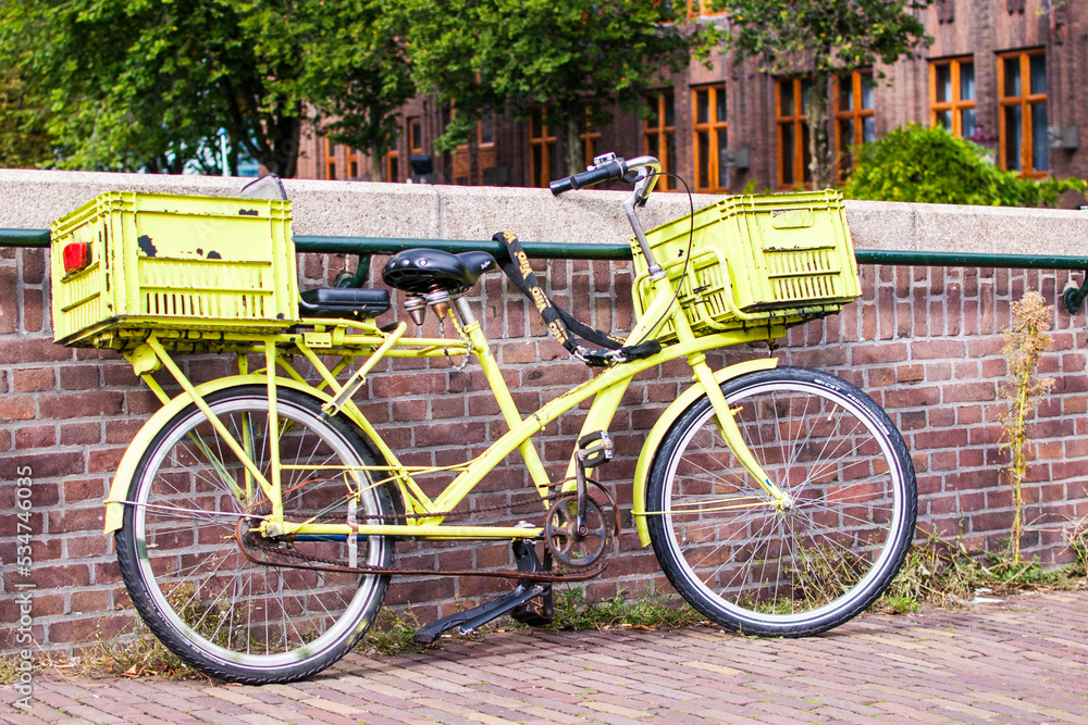 bicicleta amarilla con dos cestas aparcada en un puente sobre un canal en amsterdam, paises bajos