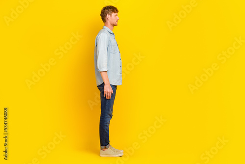 Photo of charming pretty man wear jeans shirt walking looking empty space isolated yellow color background