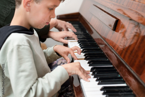 A little boy tries to play the piano, sat down next to mother and repeats the movements of playing the piano after her, he dreams of learning to play, focus on the boy's hand
