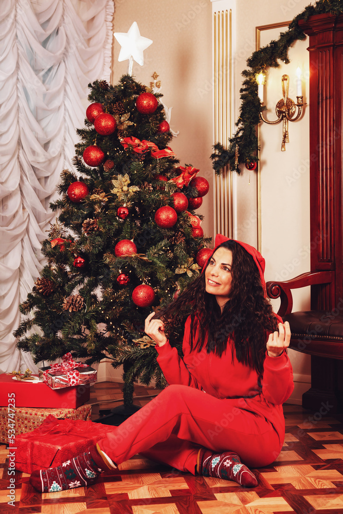 Actress woman in red cat costume posing in living room with christmas tree at cozy home, looking up. Showing atmospheric moment of Merry Christmas, Happy New Year. Copy text space