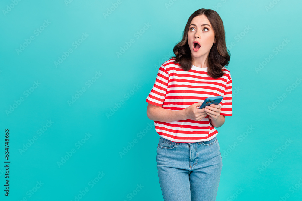 Photo of shiny impressed lady wear striped t-shirt holding modern device looking empty space isolated turquoise color background Photo of shiny impressed lady wear striped t-shirt holding modern device looking empty space isolated turquoise color background