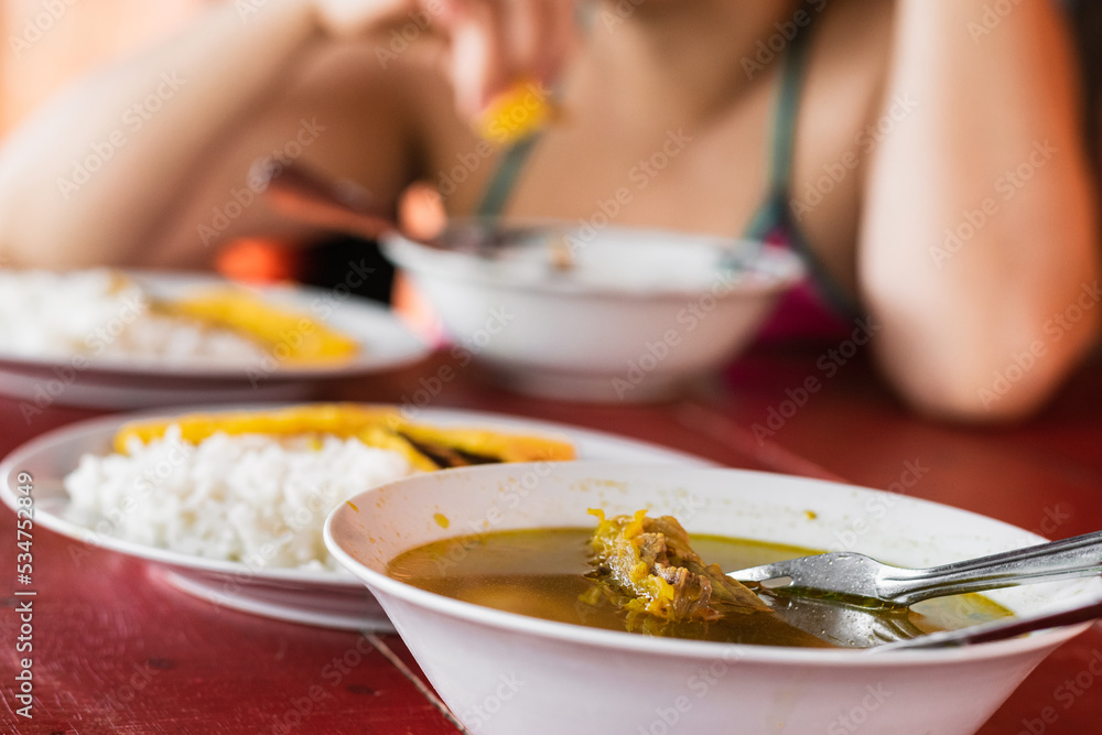 detailed view of a table served with a typical colombian breakfast, made with beef broth, in the background three white plates with rice and yellow arepa. breakfast in a colombian farm.