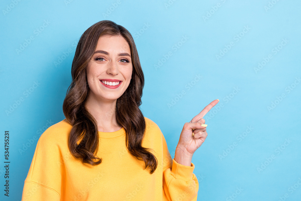 Photo portrait of charming young lady point empty space toothy smiling dressed stylish yellow clothes isolated on blue color background Photo portrait of charming young lady point empty space toothy smiling dressed stylish yellow clothes isolated on blue color background