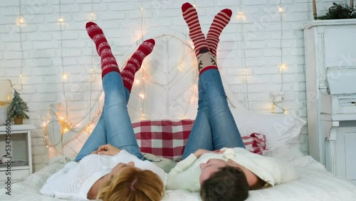 friendship and christmas home party concept - two young female friends lying down on the bed with legs up in Christmas striped socks.