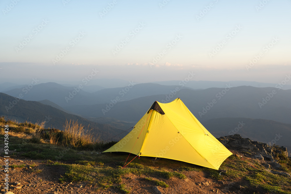 Yellow tent against the backdrop of an incredible mountain landscape during morning sunrise. Amazing highland. Tourism concept
