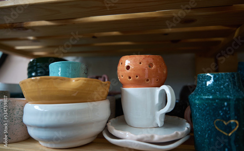 Glazed earthenware cups, plates and vases stand on wooden shelves