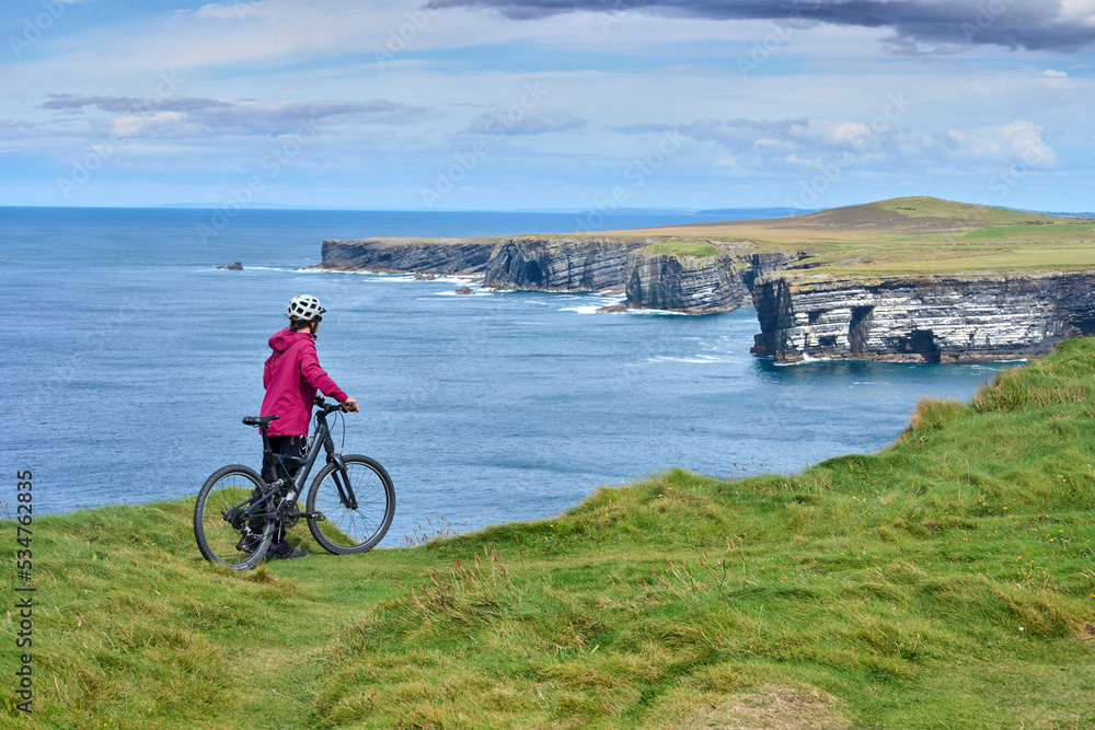 Obraz premium nice senior woman on mountain bike, cycling on the cliffs of Dunmore Head near Kilballyowen , County Limerick in the southwestern part of the Republik of Ireland
